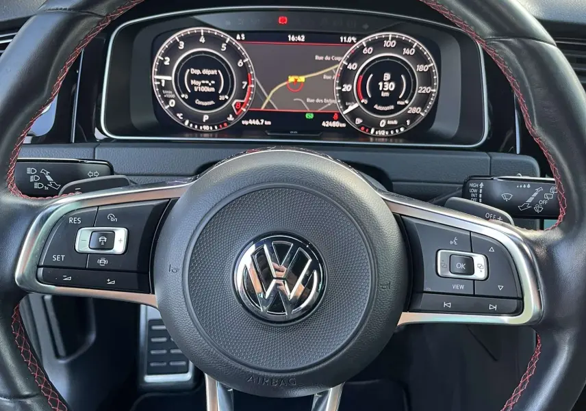 Vue rapprochée du volant cuir noir avec surpiqûres rouges et tableau de bord numérique d'une Volkswagen Golf GTI Performance.