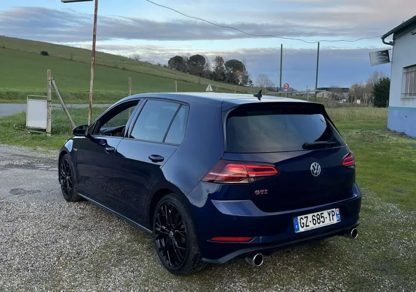 Volkswagen Golf VII GTI Performance bleu lapiz métal vue 3/4 arrière droit sur un chemin gravillonné.