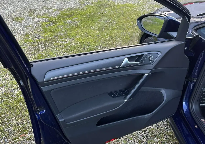 Porte avant gauche ouverte d'une Volkswagen Golf VII GTI Performance bleu lapiz, montrant les commandes de vitre et le miroir extérieur.
