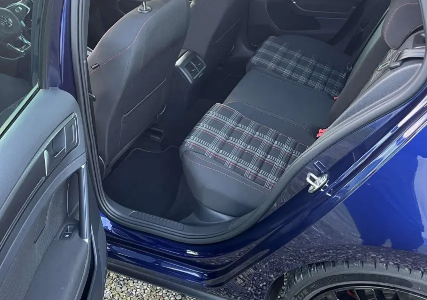 Vue intérieure arrière côté gauche d'une Volkswagen Golf VII GTI Performance bleu lapiz, sièges arrière à motif tartan et jantes noires visibles.