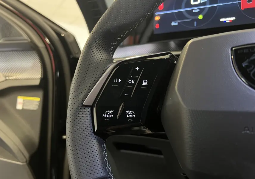 Gros plan sur la partie gauche du volant noir perforé du Peugeot 5008 2025 avec commandes d'assistance et limiteur de vitesse.