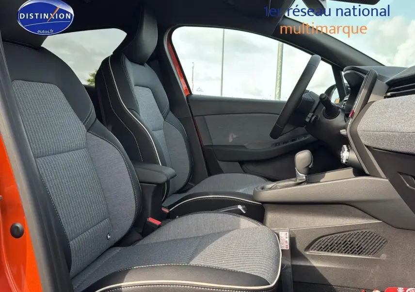 Intérieur avant de la Renault Clio V orange Valencia, sièges sport gris avec surpiqûres blanches et accoudoir central.