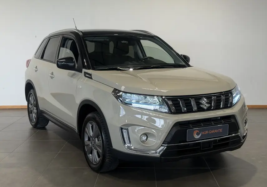 Suzuki Vitara beige 2023 vue 3/4 avant droit avec toit noir et calandre chromée dans un showroom.