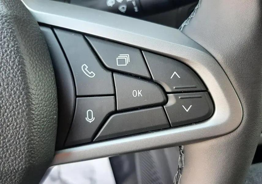 Gros plan sur les commandes multifonctions à gauche du volant du Dacia Duster 2025, finition Sandstone.