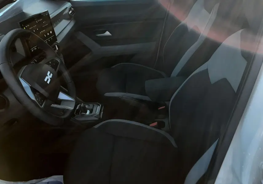 Vue intérieure côté conducteur du Dacia Duster 2025, sièges tissu gris et noir avec tableau de bord moderne.