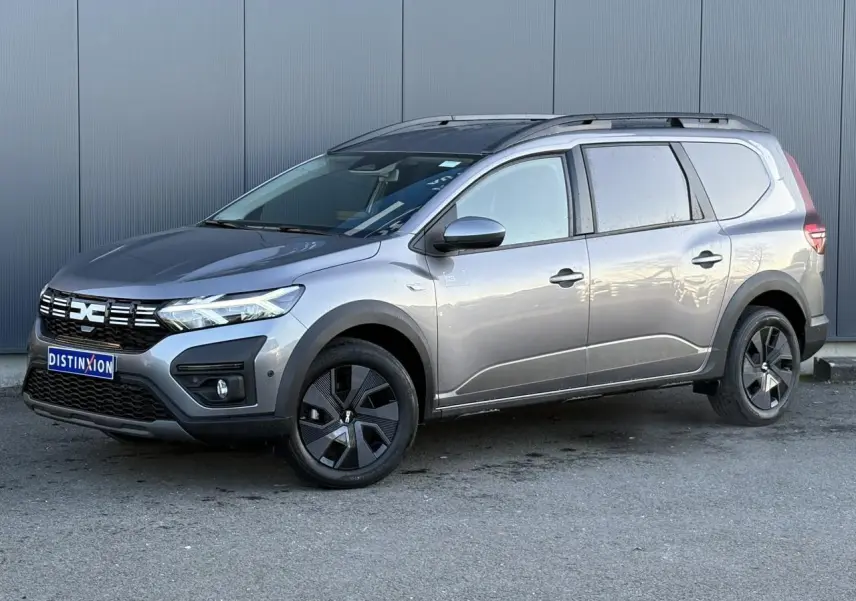 Vue 3/4 avant droit d'un Dacia Jogger Gris Schiste 2025 avec barres de toit et jantes noires distinctives.