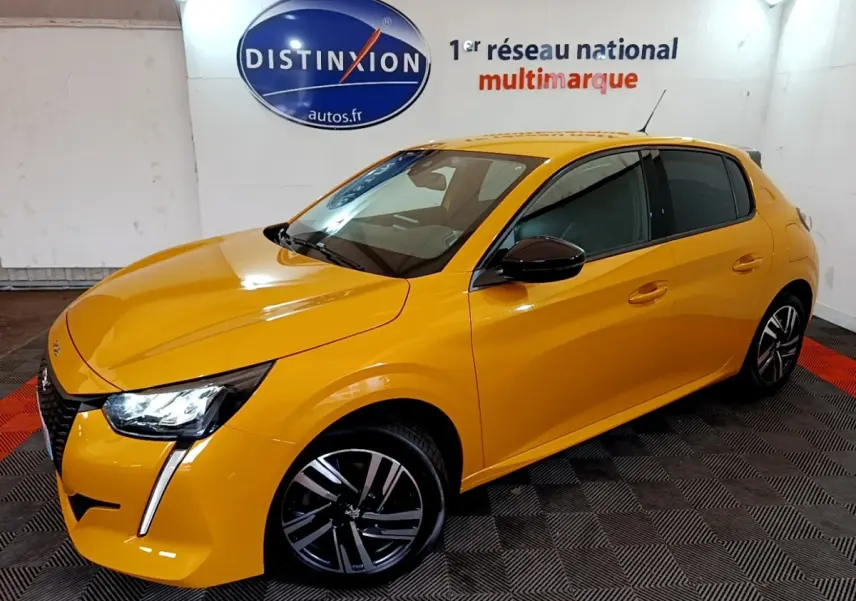Peugeot 208 jaune vue 3/4 avant droit, feux LED distinctifs et jantes alliage noires en intérieur showroom.
