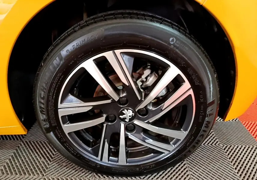 Gros plan sur la roue avant droite d’une Peugeot 208 jaune, mettant en valeur la jante alliage et le logo lion.