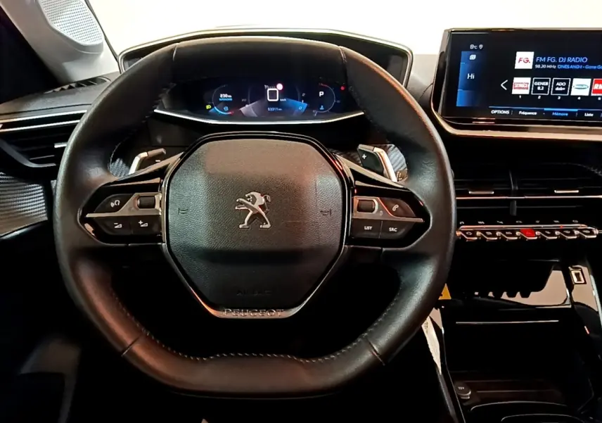 Vue rapprochée du volant cuir noir de la Peugeot 208 avec tableau de bord numérique et écran tactile central.