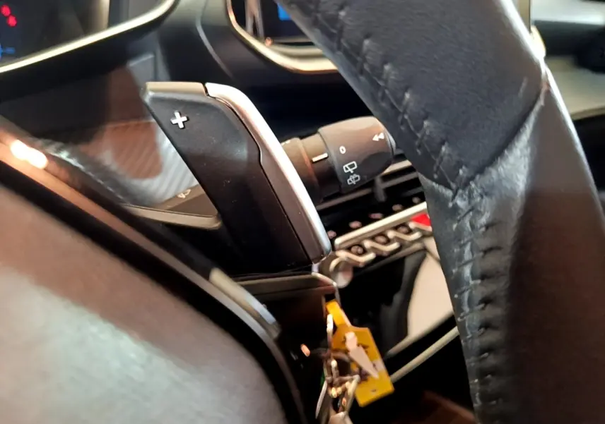 Gros plan sur la palette de changement de vitesse droite et volant cuir noir de la Peugeot 208 jaune 2023.