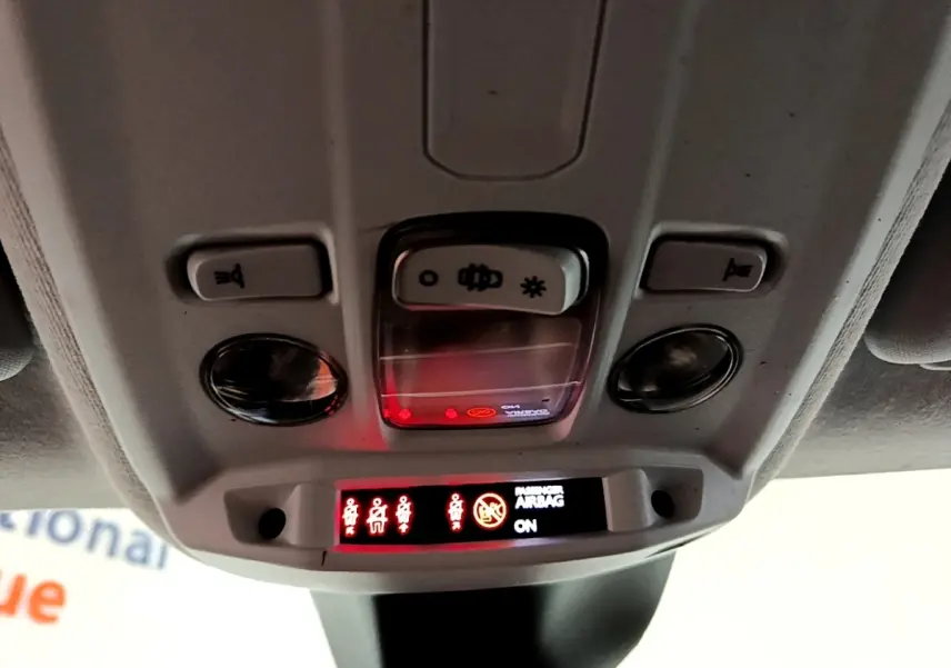 Vue en gros plan du plafonnier intérieur de la Peugeot 208 jaune, avec voyants de ceinture et airbag passager allumés.