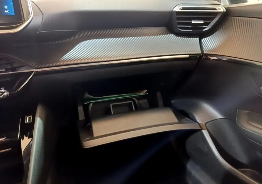 Vue intérieure côté passager de la Peugeot 208 2023 avec boîte à gants ouverte et tableau de bord noir texturé.