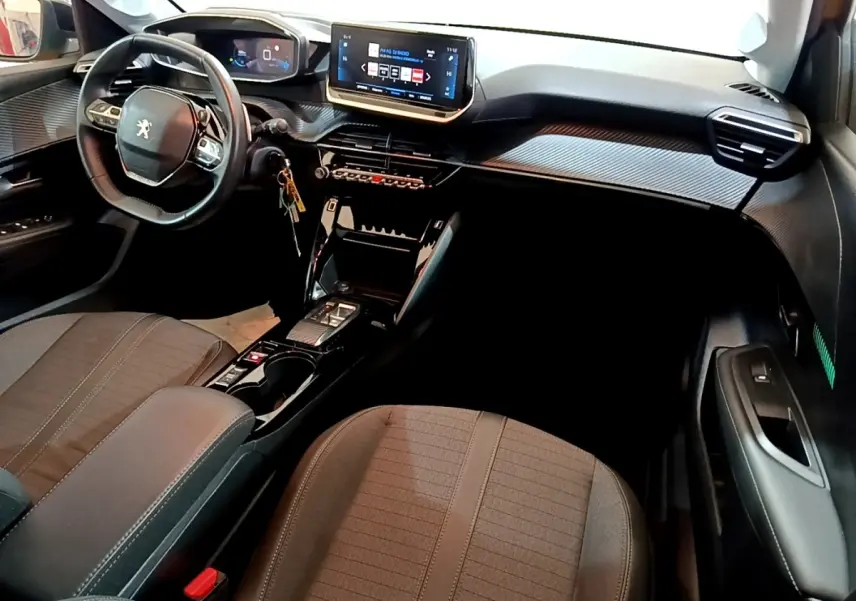 Vue intérieure avant droite du Peugeot 208 jaune 2023, montrant le volant cuir, écran tactile central et console moderne.