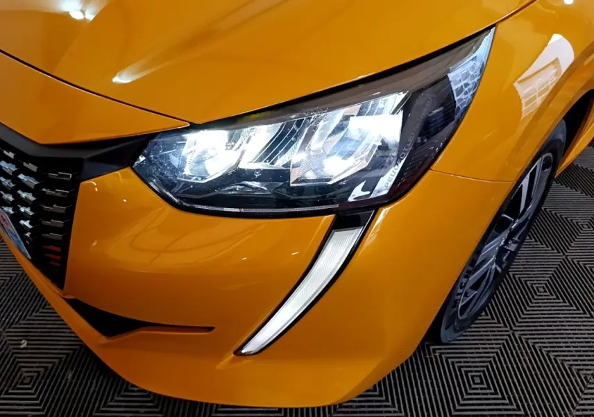 Gros plan sur l'avant droit jaune vif de la Peugeot 208 2023, mettant en valeur son phare LED et la jante alliage.
