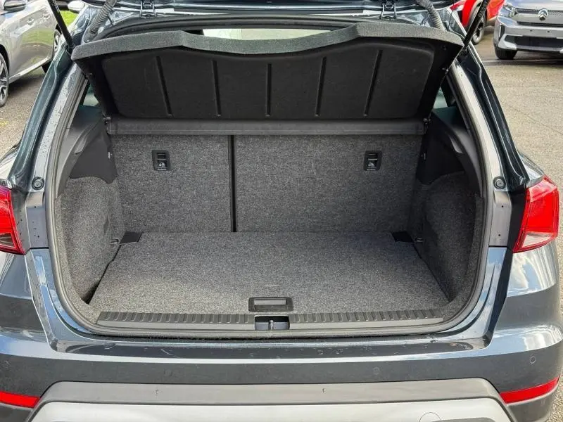 Vue arrière du coffre ouvert d'un SEAT Arona 2025 Bleu Saphir Métal avec toit blanc, montrant l'espace de chargement vide.