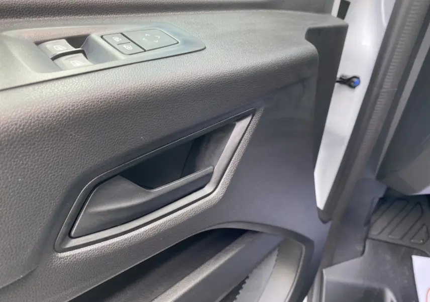 Gros plan sur la poignée intérieure et les commandes de vitre de la porte avant gauche du Renault Master blanc.