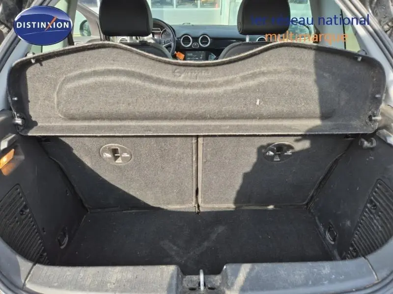 Vue intérieure du coffre ouvert d'une Opel Adam marron, montrant la banquette arrière rabattable et la tablette cache-bagages.