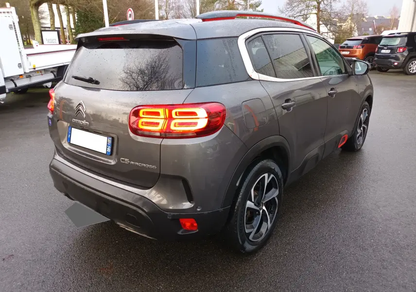 Vue 3/4 arrière droite d'un Citroën C5 Aircross gris platinium avec feux arrière allumés et jantes bi-ton.