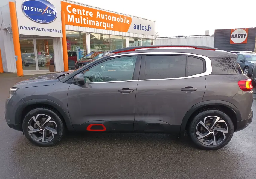 Profil côté gauche d'un Citroën C5 Aircross gris platinium avec jantes bi-ton et inserts rouges sur bas de caisse.
