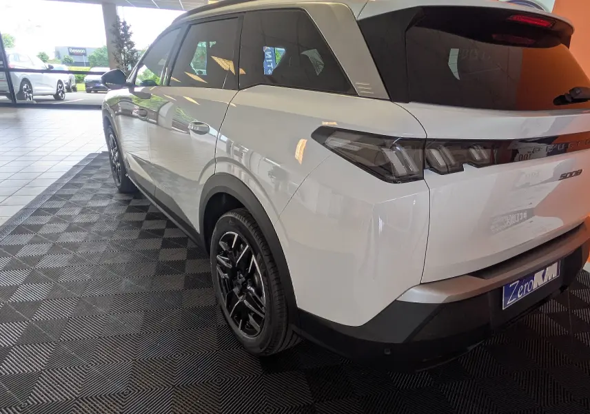 Vue 3/4 arrière droite du Peugeot 5008 blanc Okenite avec jantes alliage noires et vitres teintées en showroom.