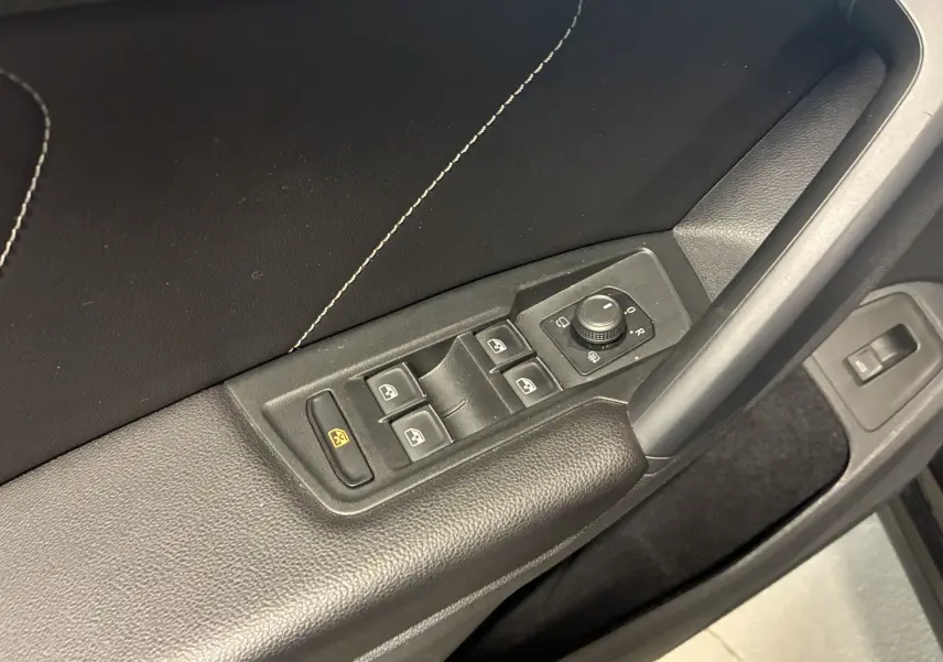 Gros plan sur la commande des vitres et rétroviseurs côté conducteur en plastique noir avec surpiqûres blanches, intérieur Volkswagen Tiguan noir.