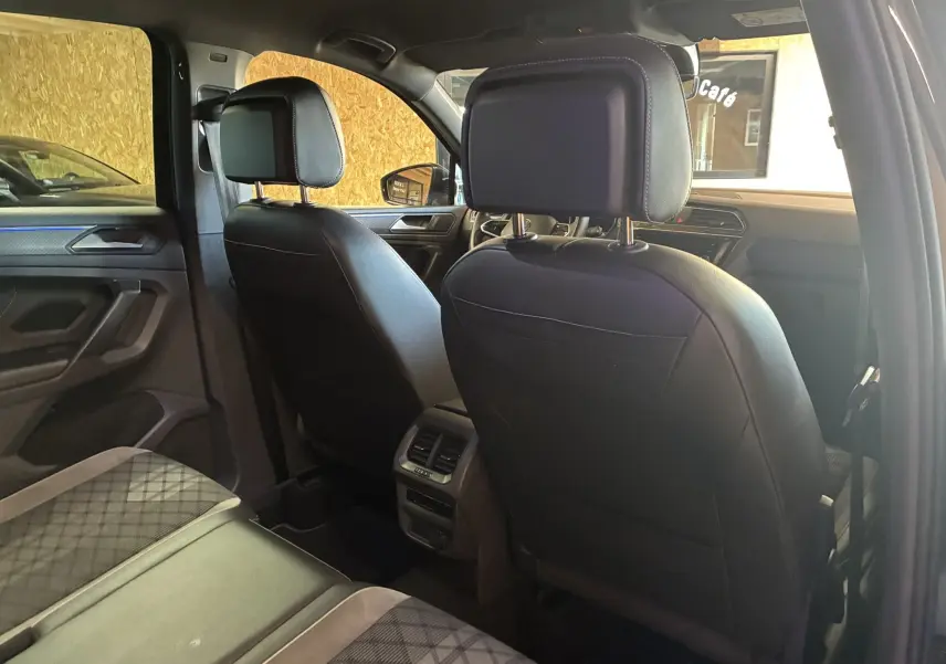 Vue intérieure arrière du Volkswagen Tiguan 2.0 TDI noir, montrant sièges avant en cuir noir et banquette tissu à motifs.