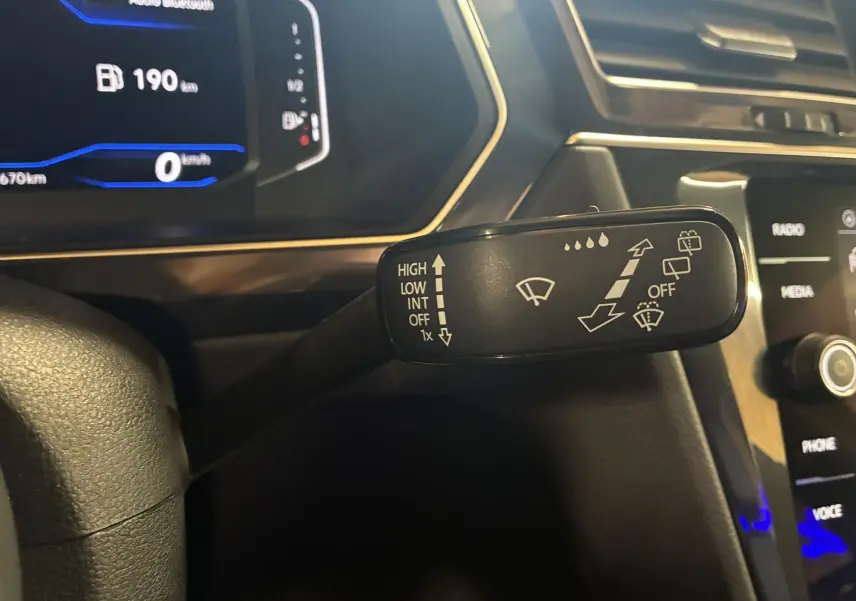 Gros plan sur la commande des essuie-glaces du Volkswagen Tiguan noir, avec tableau de bord numérique en arrière-plan.