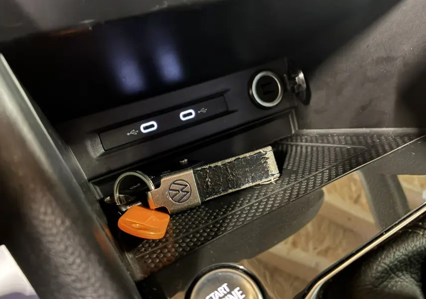 Gros plan sur la console centrale du Volkswagen Tiguan noir, avec clé VW, ports USB et bouton start engine visible.