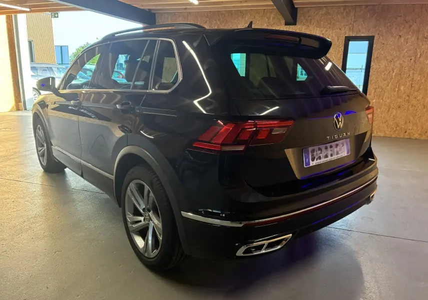 Volkswagen Tiguan noir en 3/4 arrière droit, avec jantes alu et double sortie d'échappement chromée visible en intérieur garage.
