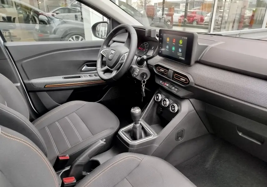 Intérieur côté conducteur de la Dacia Sandero Stepway 2021, tableau de bord moderne avec écran tactile et sièges tissu gris.
