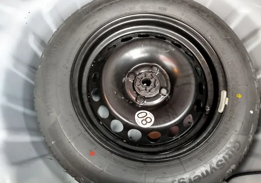 Pneu de secours noir avec jante acier circulaire, visible dans le coffre d'une Dacia Sandero Stepway blanche.