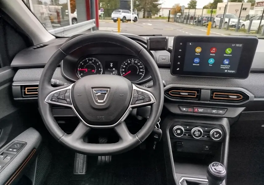 Vue intérieure du tableau de bord de la Dacia Sandero Stepway blanche, avec volant multifonction et écran tactile central.