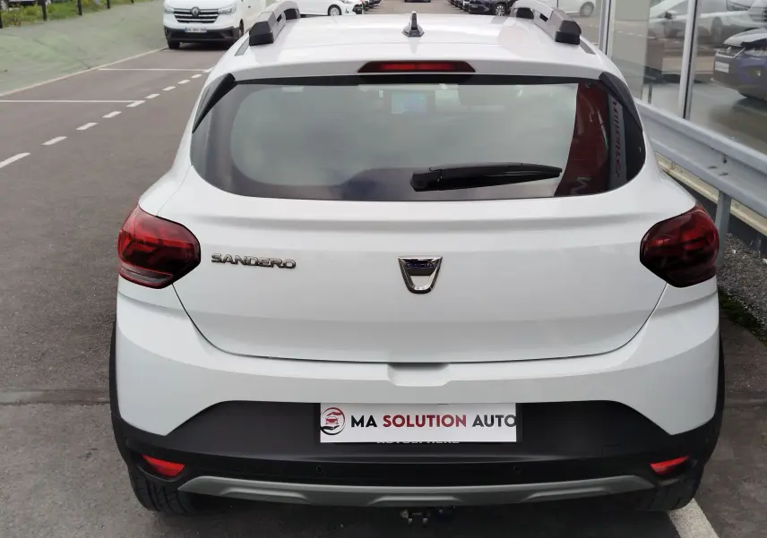 Vue arrière d'une Dacia Sandero Stepway blanche glacier avec feux arrière rouges et barres de toit noires.