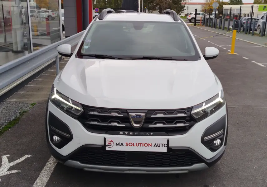 Vue frontale d'une Dacia Sandero Stepway blanche glacier avec calandre noire et feux LED allumés.