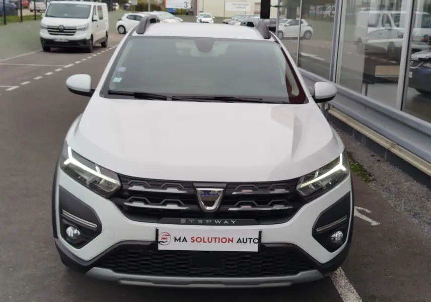 Vue frontale d'une Dacia Sandero Stepway blanche glacier avec feux LED allumés et calandre noire marquée Stepway.