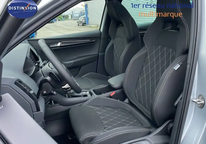 Intérieur avant du Skoda Karoq gris argent 2025, sièges sport noirs avec surpiqûres blanches et volant cuir multifonction.