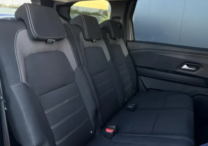 Vue latérale intérieure sur les sièges noirs du rang 2 du Dacia Jogger 2025, finition Expression avec surpiqûres blanches.