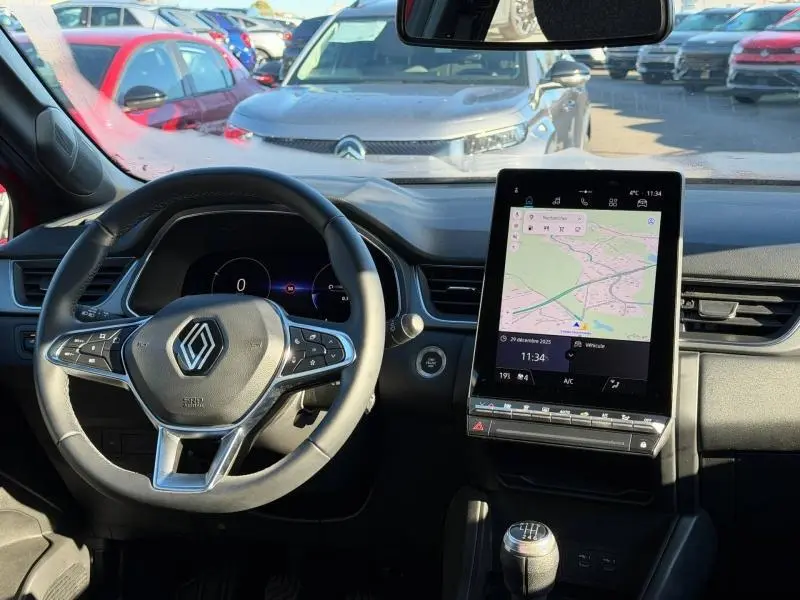 Vue intérieure du tableau de bord du Renault Captur 2025 avec volant multifonction, écran tactile vertical et levier de vitesses manuel.