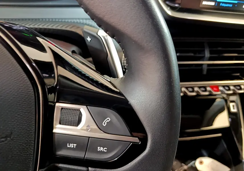 Gros plan sur le volant cuir multifonctions du Peugeot 2008 2022, avec commandes audio et palette de changement de vitesse.