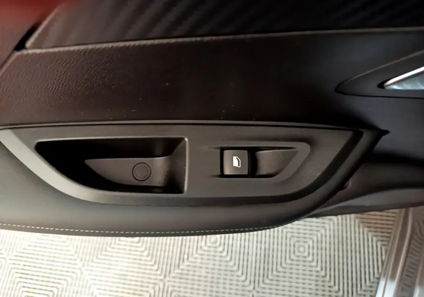 Gros plan sur la commande d'ouverture de trappe à carburant sur la porte intérieure noire d'une Peugeot 2008 gris foncé.