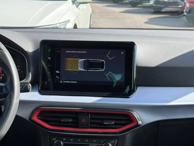 Vue intérieure du tableau de bord du SEAT Arona 2025, écran central affichant l'aide au stationnement, entouré d'aérations rouges.
