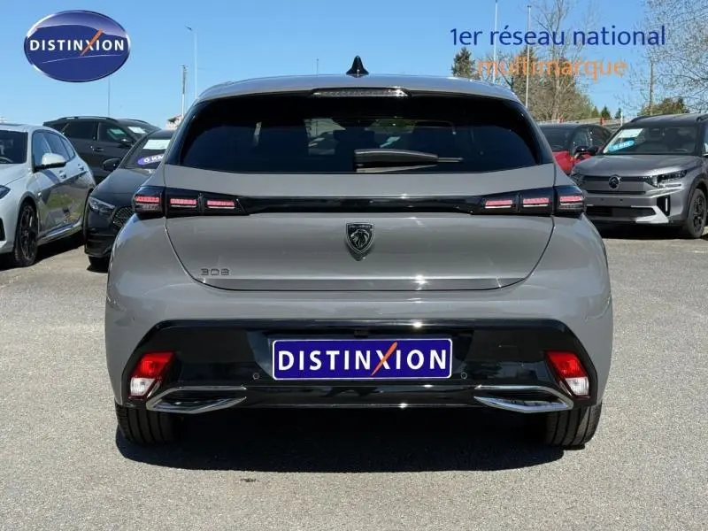 Vue arrière d'une Peugeot 308 gris 2025 avec feux LED étirés et logo lion central sur un parking.