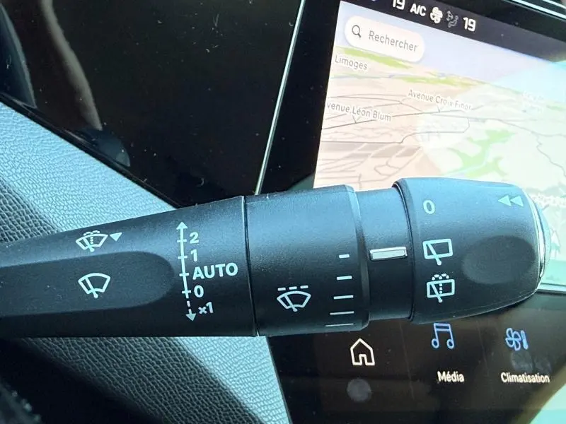 Gros plan sur la commande des essuie-glaces dans l’habitacle gris du Peugeot 308 Hybrid 2025, avec écran tactile en arrière-plan.