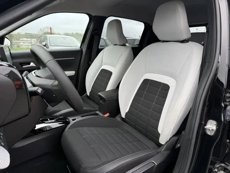 Vue intérieure côté conducteur de la Citroën C3 électrique 2025 noir Perla Nera, sièges bicolores gris clair et noir.