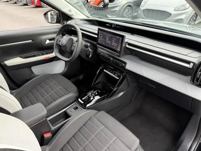 Vue intérieure côté conducteur de la Citroën C3 électrique 2025 avec tableau de bord moderne et sièges noirs.