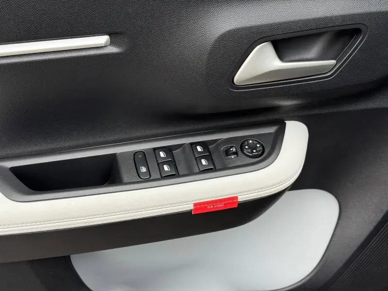 Vue rapprochée de la porte côté gauche de la Citroën C3 électrique 2025, avec commandes de vitres et garniture noire et blanche.