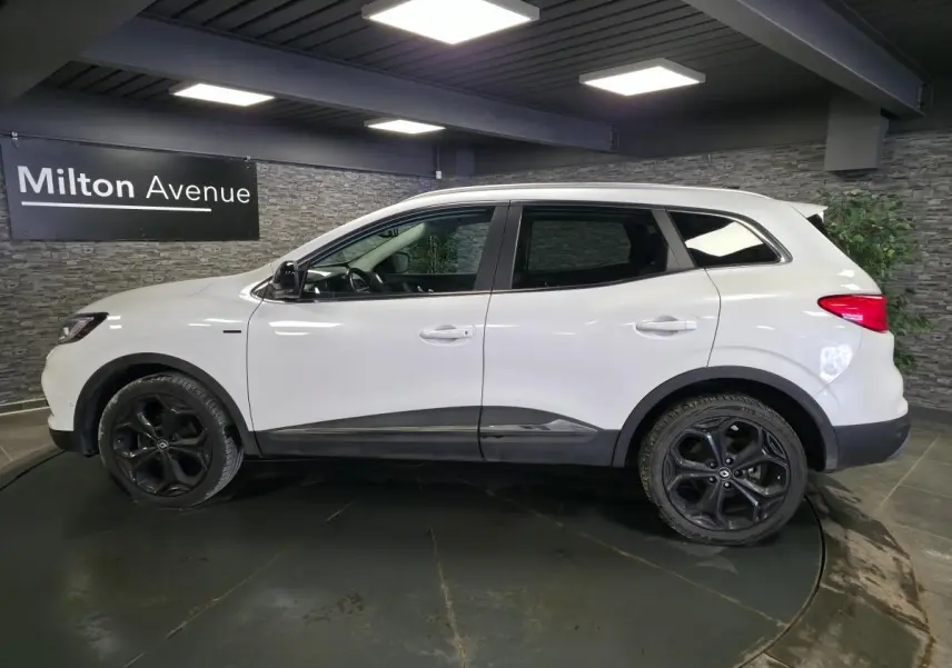 Profil gauche d'un Renault Kadjar blanc nacré avec jantes alliage noires 19'' dans un showroom intérieur.