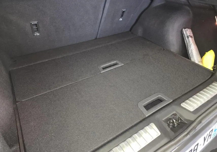 Vue du coffre fermé du Renault Kadjar blanc 2020 Black Edition, avec tapis de sol noir et accessoires rangés sur le côté droit.