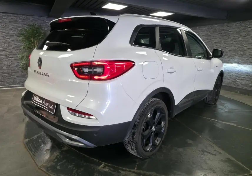 Vue 3/4 arrière droite du Renault Kadjar blanc nacré avec jantes alliage noires et toit en verre fixe dans un showroom.