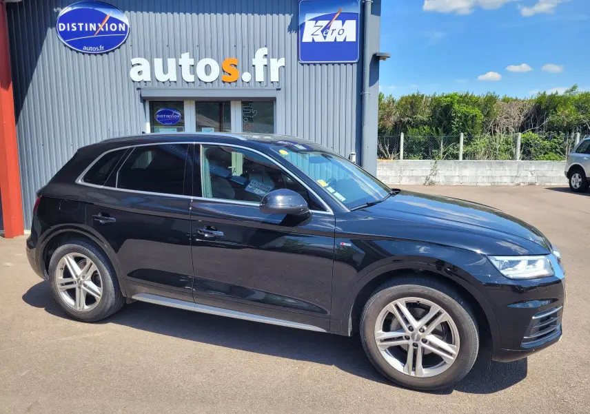 Audi Q5 noire S Line vue de profil côté gauche, garée devant un bâtiment avec enseigne autos.fr par temps ensoleillé.